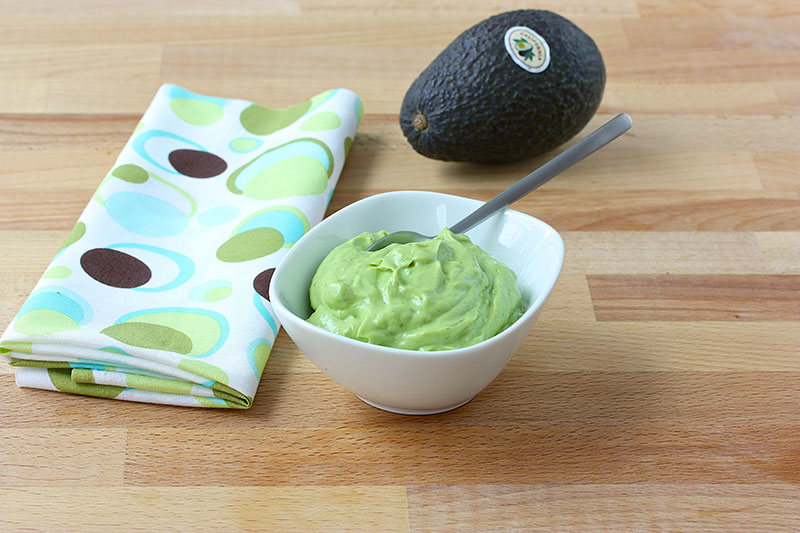 Bowl of avocado sauce next to a kitchen towel an a whole avocado