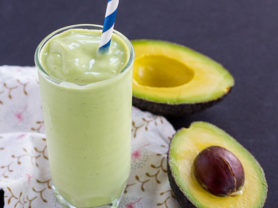 Glass of California Avocado milkshake with an avocado cut in half next to it.